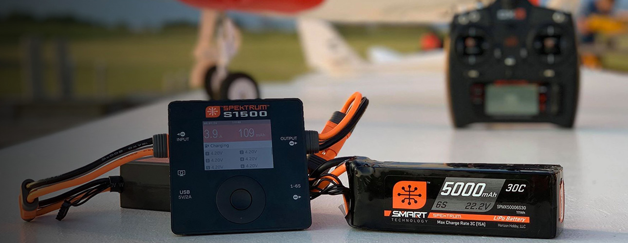 Picture of a RC plane and transmitter in the background featuring a Spektrum charger and battery.
